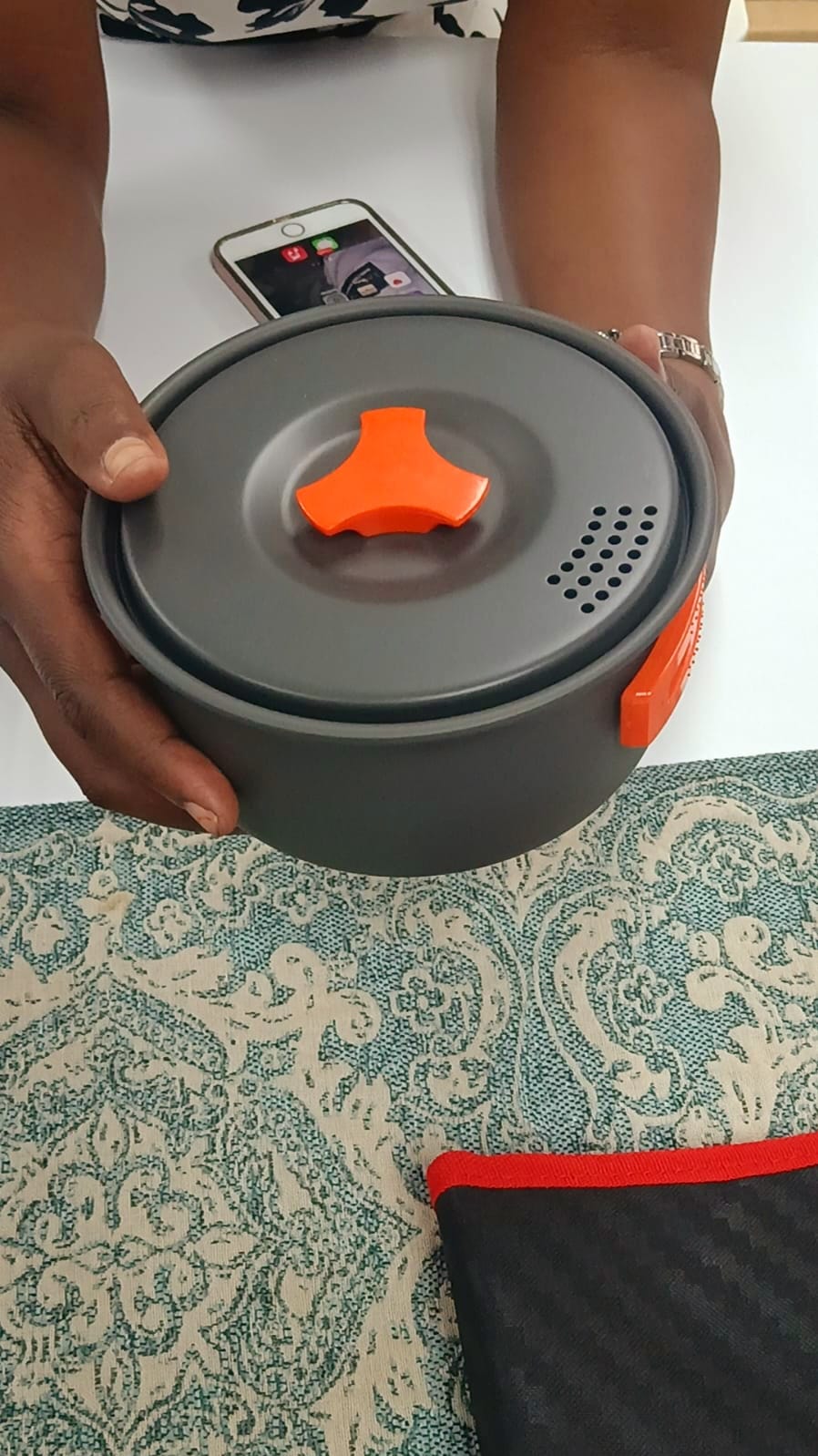 "A portable camping stove with two burners, a small cooking pot, and a frying pan set up on a picnic table in a campsite